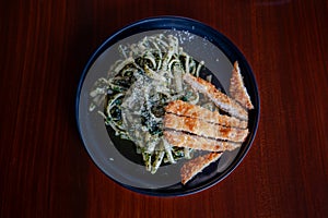 Plate of pasta in olive oil with basil and parmesan topped with tonkatsu sliced