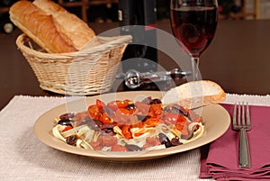 A plate of pasta puttanesca with wine and bread