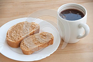 Plate with peanut butter bread and a cup of coffee on the wooden table. Close-up