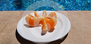 Plate with peeled mandarin slices stand near blue outdoor pool