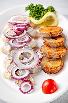 Plate of pieces of herring with fried potato,onion, tomato and lemon. Close up image with selective focus