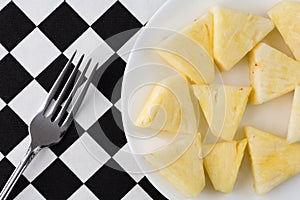 Plate of pineapple slices with a fork on a tablecloth
