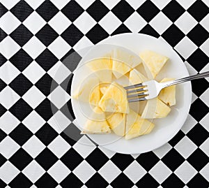 Plate of pineapple slices with a fork on a tablecloth