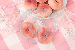 A plate of pink peach fruits on a delicate picnic tablecloth