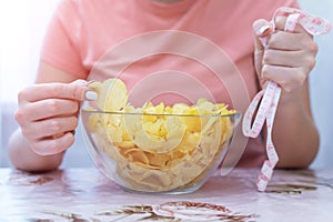 A plate of potato chips and a centimeter tape in the girl`s hands. Junk food. The concept of struggle against excess weight.