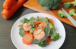 Plate of prawn stir fried with broccoli and carrot with blurry cut vegetables in background