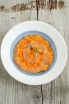 Plate with pumpkin puree and pumpkin seeds. Old wooden background. Top view, copy space