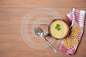 A plate of pumpkin soup, grain loaves on a red napkin and a brown wooden background .