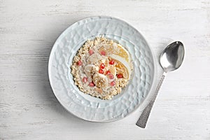 Plate of quinoa porridge with orange, banana and pomegranate seeds near spoon on white wooden background
