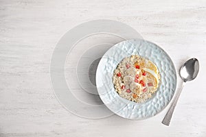 Plate of quinoa porridge with orange, banana and pomegranate seeds near spoon on white wooden background, top view.