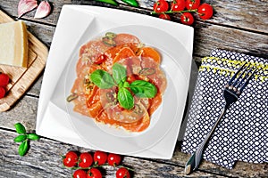 Plate with red heart ravioli with cherry tomato, mozzarella, parmesan and basil on a wood background