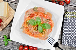 Plate with red heart ravioli with cherry tomato, mozzarella, parmesan and basil on a wood background