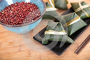 A plate of rice dumplings and a bowl of red beans on a cutting board