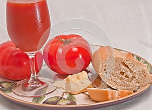 Plate with a ripe, local, freshly picked, beef steak tomatoes with a chuck of aged cheese, a section of freshly baked baguette