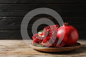 Plate with ripe pomegranates on wooden table against dark background
