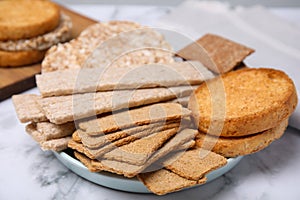 Plate of rye crispbreads, rice cakes and rusks on white marble table