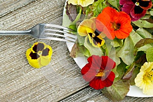 Plate of salad with edible flowers and lettuce on the wooden table