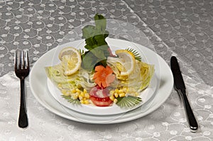 A plate of salad made of lettuce, tomato, corn, carrot, lemon and dill.