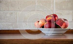 A plate with Saturn peaches on a wooden table in the kitchen. Peaches on a kitchen table against a brick wall background with copy