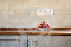 A plate with Saturn peaches on a wooden table in the kitchen. Peaches on a kitchen table against a brick wall with power sockets