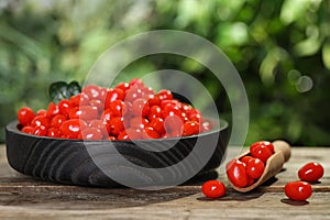 Plate and scoop with fresh goji berries on wooden table against blurred background