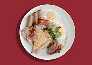 A plate with scrambled eggs, bacon, beans, sausages, tomatoes and croutons on a red background.
