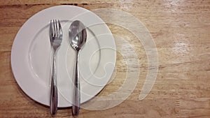 Plate and silverwear including spoon and fork on wood background