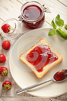 Plate with slice of bread and delicious strawberry jam on white wooden table