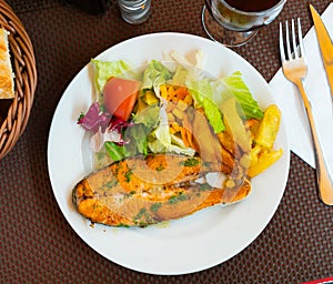 On plate, slice of fried salmon garnished with French fries and salad of fresh vegetables