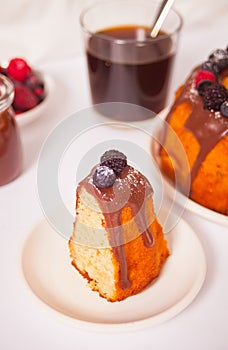 Plate with slice of tasty homemade vanilla bunt cake with berries and glass of coffee on the background