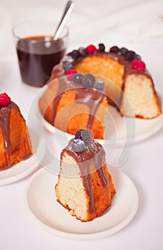 Plate with slice of tasty homemade vanilla bunt cake with berries and glass of coffee on the background