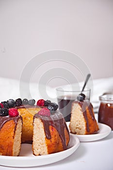 Plate with slice of tasty homemade vanilla bunt cake with berries and glass of coffee on the background