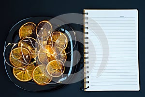 Plate with slices of dried orange and burning garland, Christmas home decor copy space on black background