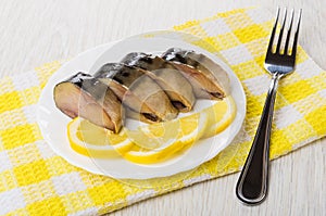 Plate with slices of smoked mackerel, lemon on napkin, fork