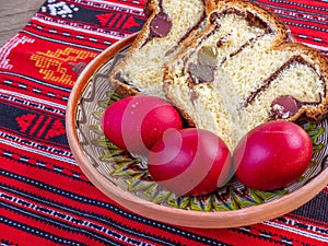 Plate with slices of traditional easter sweet bread or cozonac and red painted eggs, romanian easter tradition