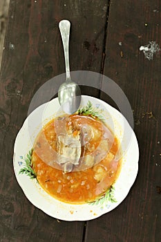 Plate with soup containing meat with bone, potato rice and tomato sauce