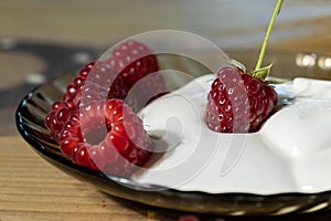 On a plate of sour cream and raspberries close-up delicious dessert