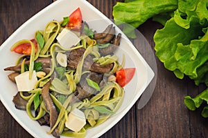 Plate of spaghetti dough with spinach and oyster mushrooms. Italian cuisine, Italian recipes. Wooden background. Top view. Close-u