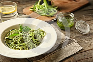 Plate of spaghetti with zucchini and pesto sauce on wooden table