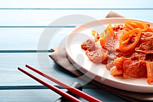 Plate of spicy cabbage kimchi with chili pepper and chopsticks on light blue wooden table, closeup