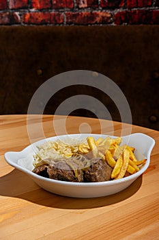 A plate of stewed black pork cheeks, paired with white rice and crispy French fries, displayed in a restaurant setting.