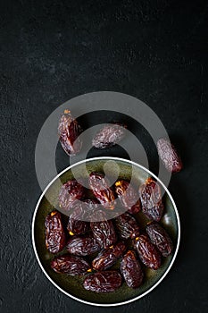 Plate with sweet dates on a black background, flat lay