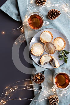 A plate with sweet mince pies and cups with black tea and Christmas cones on the table flat lay with copy space
