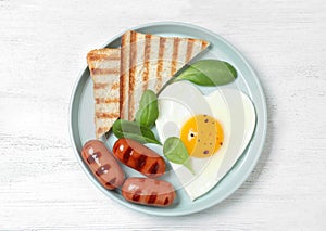 Plate of tasty breakfast with heart shaped fried egg on wooden table, top view