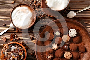 Plate with tasty chocolate truffles and cups of cappuccino on wooden table