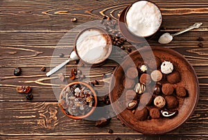 Plate with tasty chocolate truffles and cups of cappuccino on wooden table