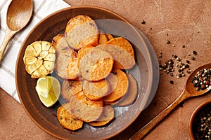 Plate with tasty cooked sweet potatoes, rosemary, sauce and spices, herbs on textured background