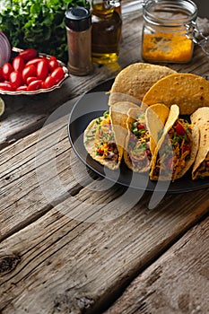 Plate with tasty mexican tacos on rustic wooden table with ingredients for cooking background. Concept of traditional meal.