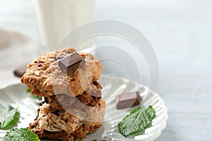 Plate with tasty oatmeal cookies, chocolate and mint leaves on table