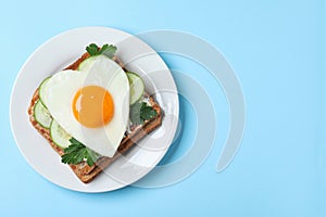 Plate of tasty sandwich with heart shaped fried egg on blue background, top view. Space for text